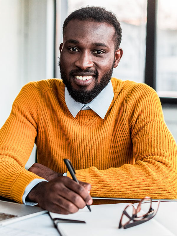 Principal wearing a yellow shirt smiles at the camera as he signs a paper