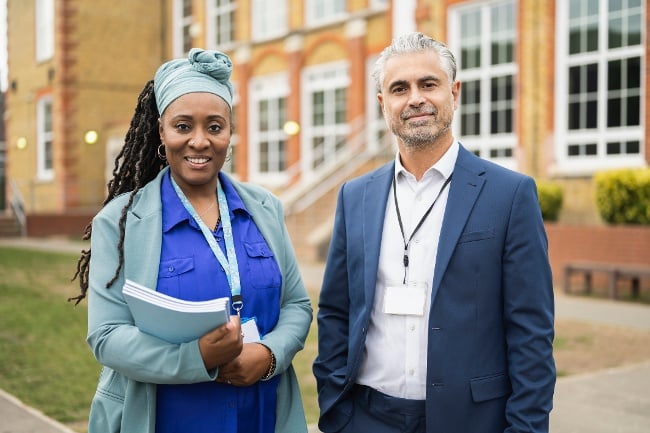 male and female school leaders standing outside of a  school building