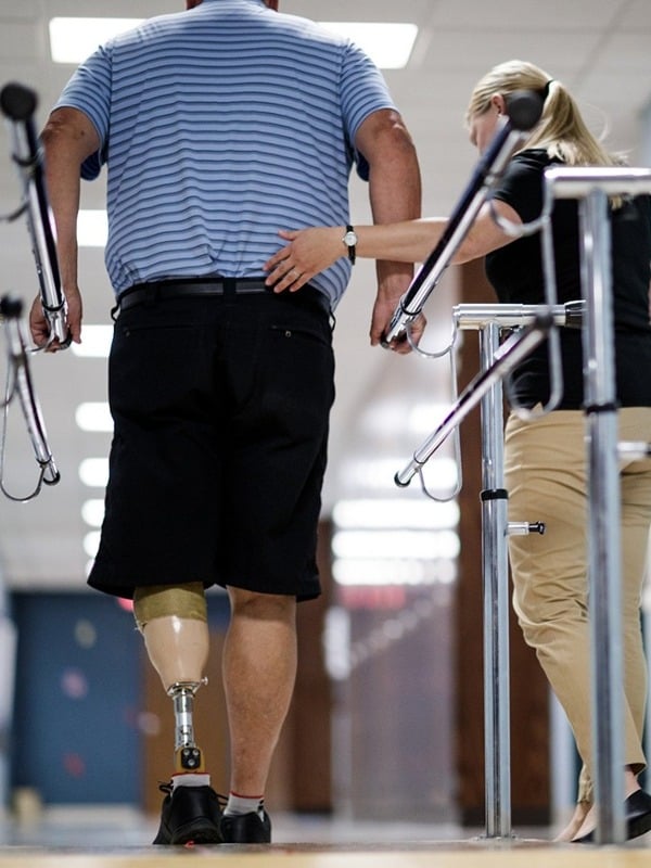 Occupational therapist assists man with a prosthetic leg walk